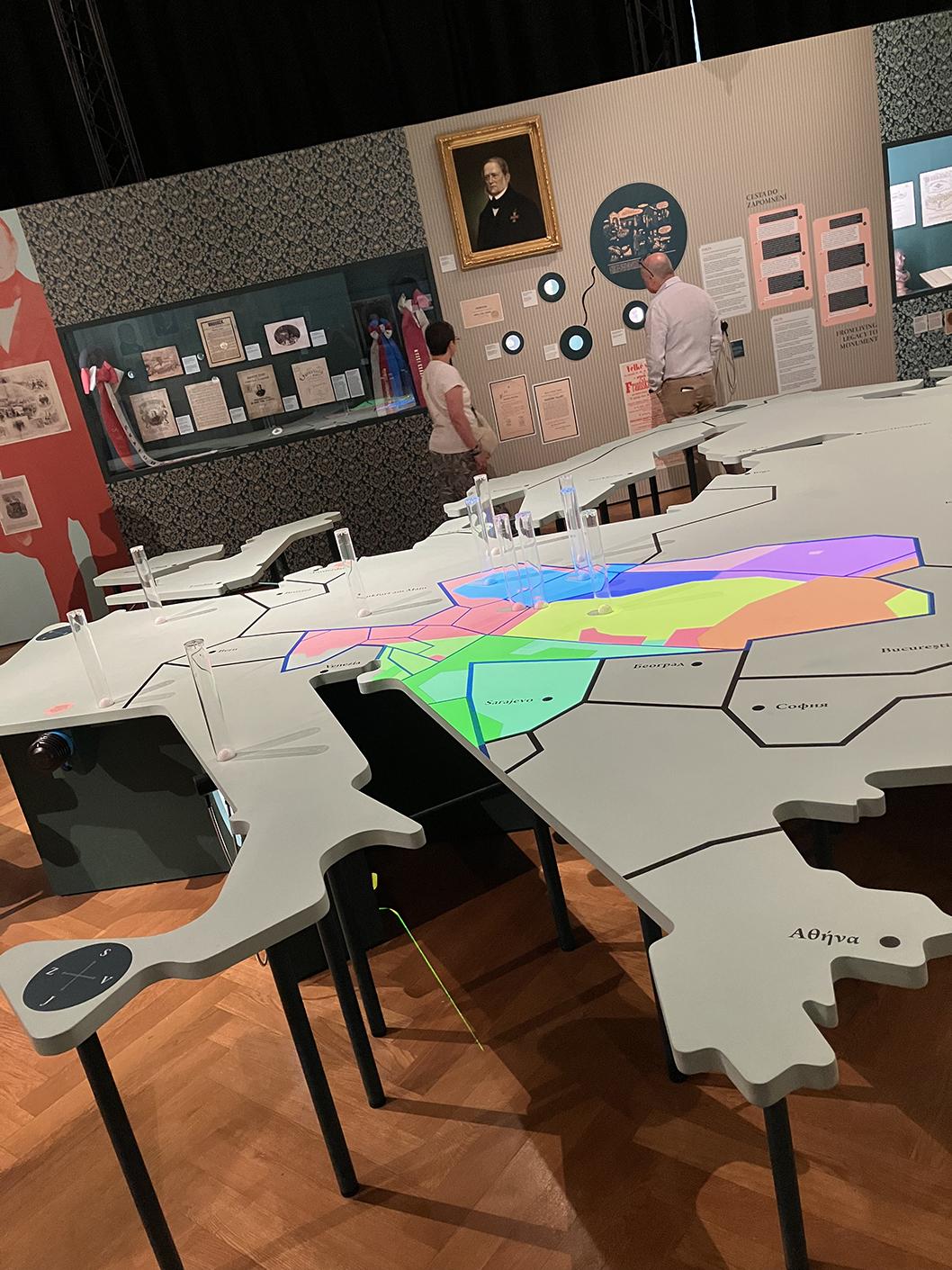 A large gray table cut into the shape of the map of Europe, showing political boundaries (as of 1878), with projected colors for the different ethnic gropus within the Austro-Hungarian empire, on display in Prague's National Museum
