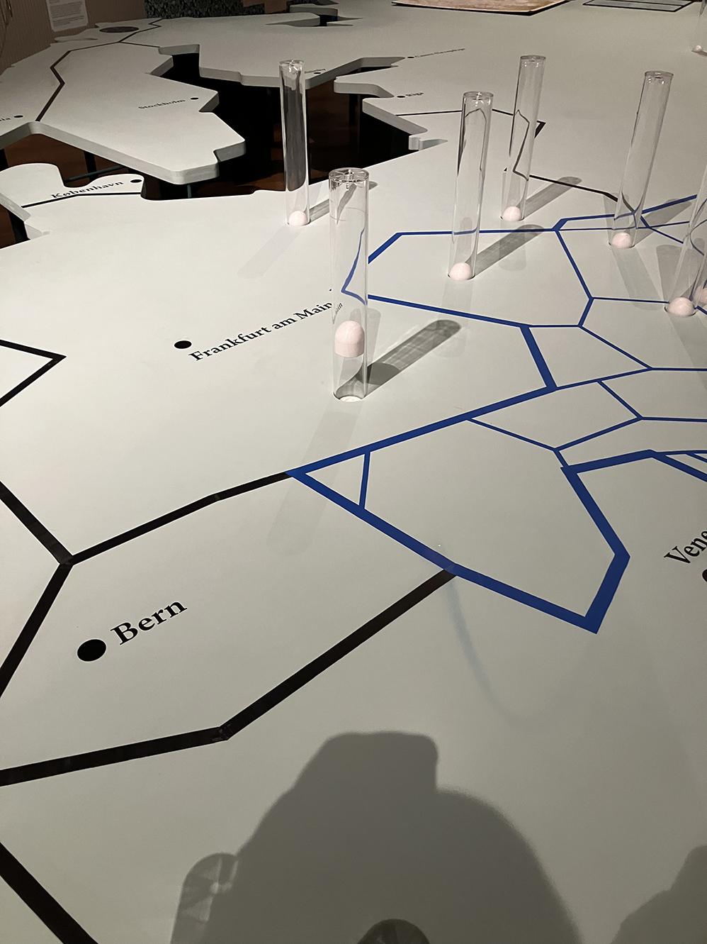 Detail of the large table cut out as a map of Europe, showing some of the transparent pneumatic tubes, one with the golf ball rising to mark the site of Munich