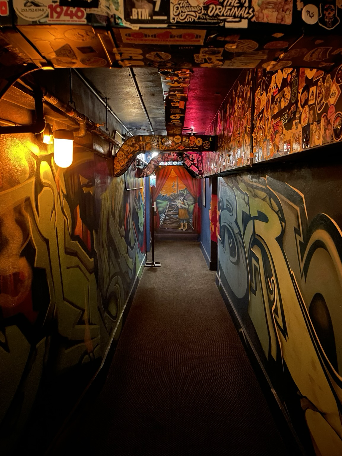Interior hallway of McMenamins in Tacoma, showcasing vibrant graffiti on the walls under a glowing light fixture.